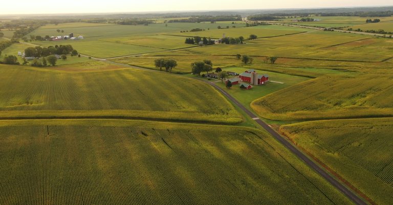 An overview of multiple plots of farmland. There is a farm with many barns sitting right in between all of them.